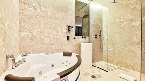 A modern bathroom with a large bathtub, a glass shower enclosure, and marble walls.