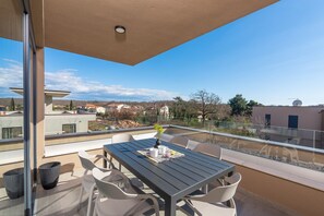 A balcony with a table and chairs, a potted plant, and a view of houses and trees. - Luxurious Apartment with Jacuzzi, Sea View, and Balcony in Istria (Brtonigla)