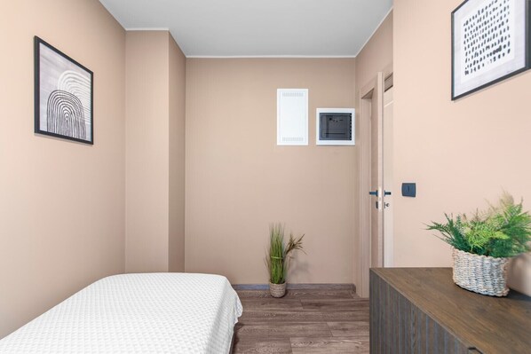A bedroom with a bed, a potted plant, a dresser, and a wall-mounted air conditioning unit.