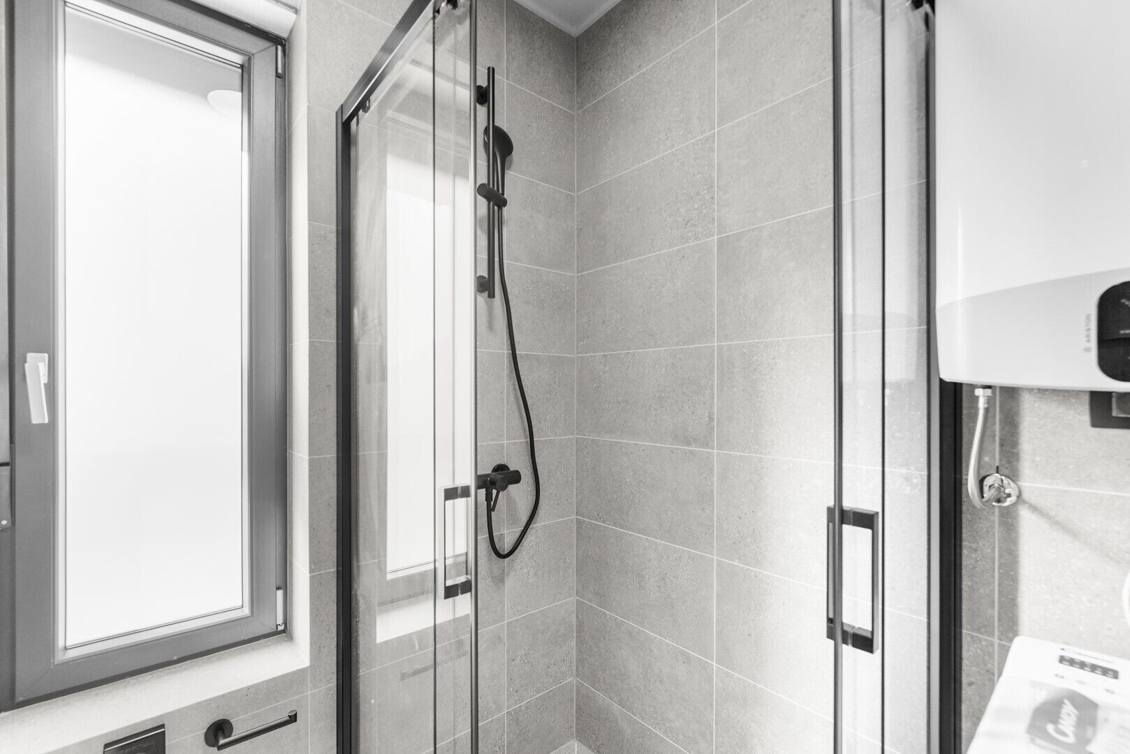 A modern bathroom with a glass shower enclosure, tiled walls, and a window.