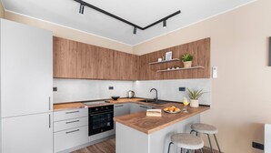 A modern kitchen with wooden cabinets, a built-in oven, a sink, and a bar area with stools. - Exclusive Ground-Floor Apartment with Private Pool and Terrace in Istria (Brtonigla)