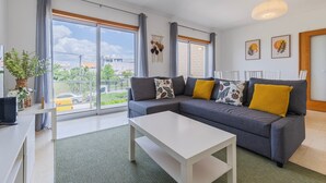 Een moderne woonkamer met een grijze bank, een witte salontafel en grote ramen met uitzicht op het omliggende landschap.
