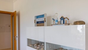 Een witte kast met glazen deuren, waarin schelpen en decoraties met een nautisch thema staan uitgestald.