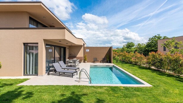 A modern hotel with a swimming pool, outdoor seating, and a well-maintained lawn.