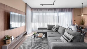 A modern living room with a sectional sofa, a flat-screen TV mounted on the wall, a round coffee table with books and a plant, and a dining area with a table and chairs. - Ground-Floor Apartment with Private Pool and Terrace in Istria, 150 Meters from the Sea (Brtonigla)