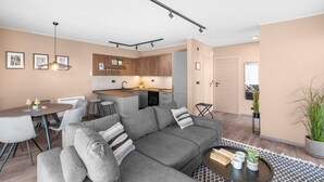 A modern living room with a grey sofa, a dining table with two chairs, a kitchen area with wooden cabinets, and a small island with a sink. - Ground-Floor Apartment with Private Pool and Terrace in Istria, 150 Meters from the Sea (Brtonigla)