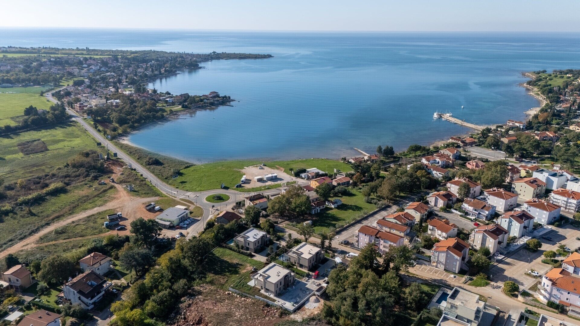 Ein Luftbild einer Küstenwohngegend mit Häusern, einem Yachthafen und einer Straße, die zum Meer führt.