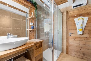 A modern bathroom with a wooden vanity, a glass shower enclosure, and a towel hanging on a wooden door. - Newly Renovated Rustic Apartment in the Heart of Novigrad's City Center, Just Steps from the Beach (Novigrad)