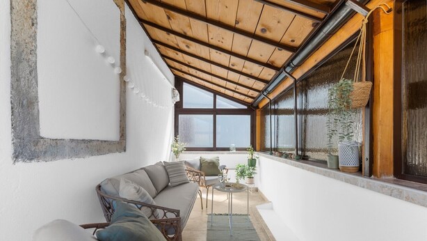 Een knus interieur met houten plafond, een bank, een klein tafeltje met drankjes en potplanten.