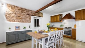 Een keuken met een stenen muur, houten keukenkastjes, een wit aanrecht en een eettafel met stoelen.