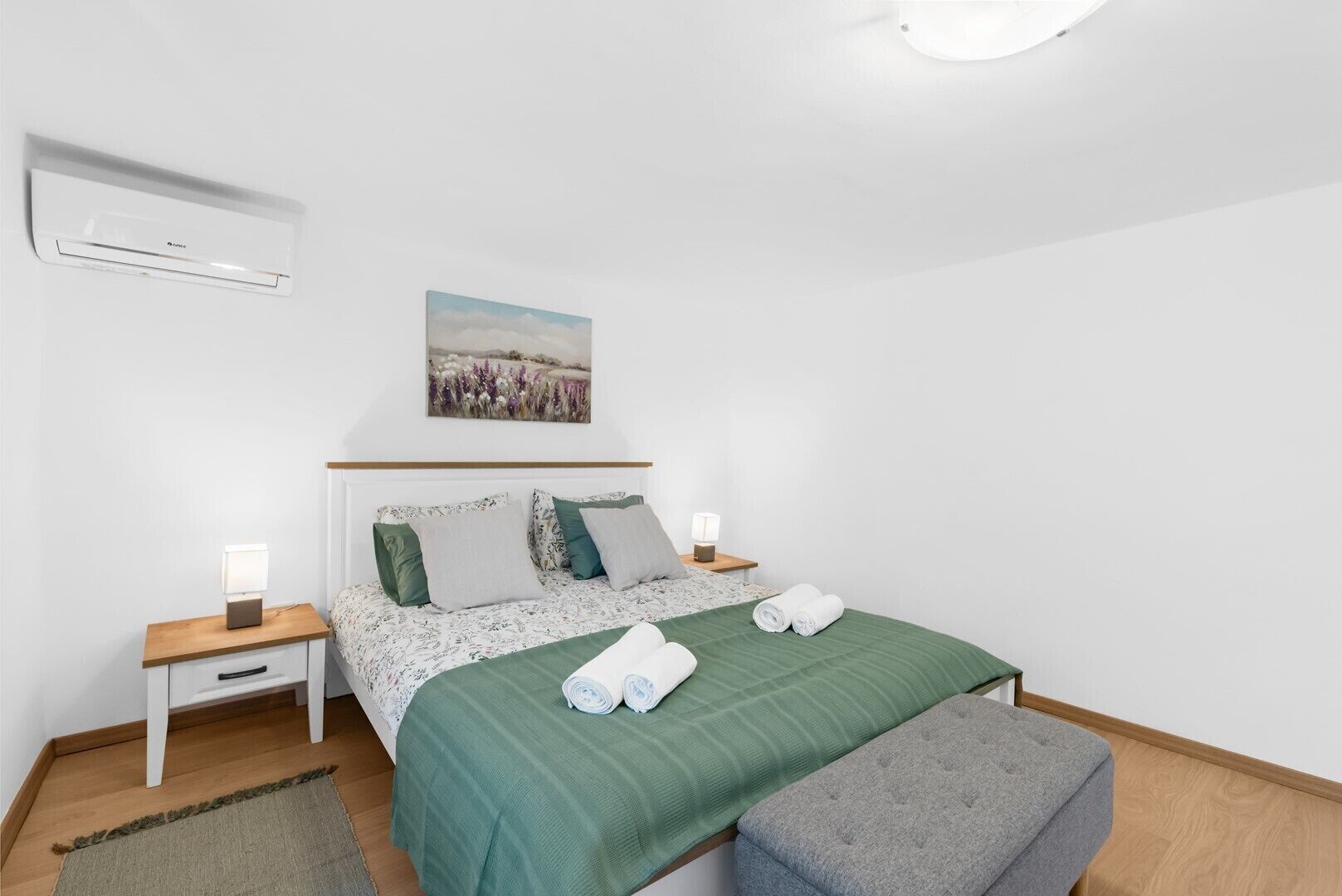 Een keurig opgemaakt slaapkamer met een bed, nachtkastjes, een wandairco en een schilderij.