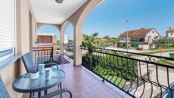 A balcony with a table and chairs, a view of the street, and a stop sign.
