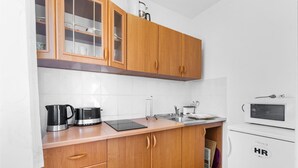 A compact kitchen with wooden cabinets, a stainless steel sink, a kettle, a microwave, and a toaster.