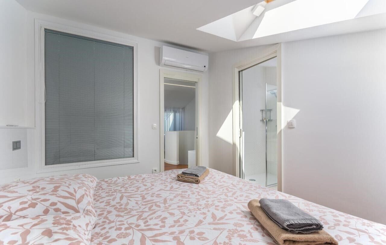 Une chambre avec un grand lit, une lucarne, un dressing et une porte de douche en verre.