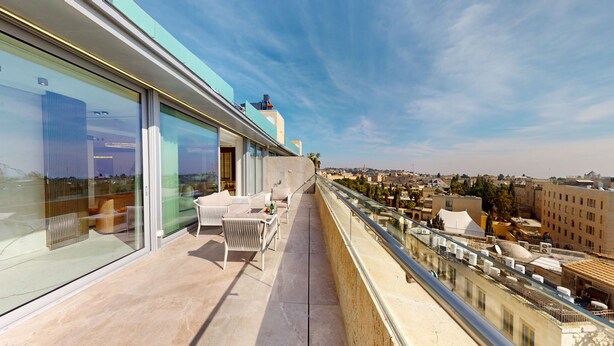 A balcony with a seating area, glass walls, and a view of the cityscape. - Exclusive King David Penthouse-4BR &breathtaking views! (Jerusalem)