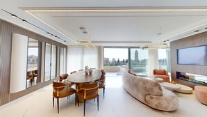A modern living room with a round dining table, comfortable seating, a large sofa, and a television. - Exclusive King David Penthouse-4BR &breathtaking views! (Jerusalem)