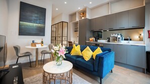 Ein modernes Wohnzimmer mit einem blauen Sofa, einem runden Tisch und einer Küchenzeile mit grauen Schränken.