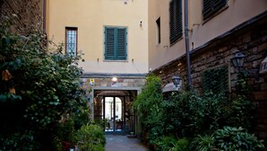 An outdoor courtyard with a stone pathway, potted plants, and a building entrance with a door and windows. - PONTE VECCHIO VIEW FLORENCE (Firenze)