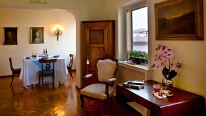 A dining area with a table set for two, a wooden chair, a desk with a vase of flowers, and a window with a view. - PONTE VECCHIO VIEW FLORENCE (Firenze)