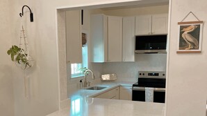 A modern kitchen with white cabinets, a large island, two brown bar stools, and a hanging plant. - Beautifully renovated,  walkable home in Charleston - close to everything! (Charleston)