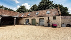 A two-story stone building with a gravel courtyard, multiple windows, and a covered area with outdoor furniture. - Charming Barn Retreat near Cotswolds & Bath (Bath)