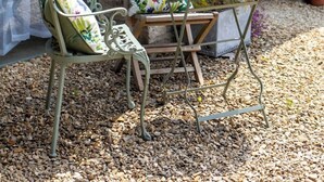An outdoor seating area with a table and chairs, a potted plant, and a stone building with a green door in the background. - Charming Barn Retreat near Cotswolds & Bath (Bath)