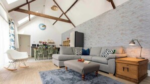 A spacious living room with a grey sofa, wooden side table, and a blue rug. - Charming Barn Retreat near Cotswolds & Bath (Bath)
