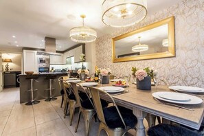 Un comedor con una mesa larga, taburetes de bar y una cocina al fondo.