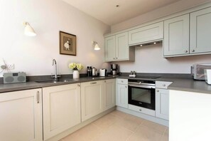 Una cocina moderna con gabinetes de colores claros, encimera negra y electrodomésticos básicos.