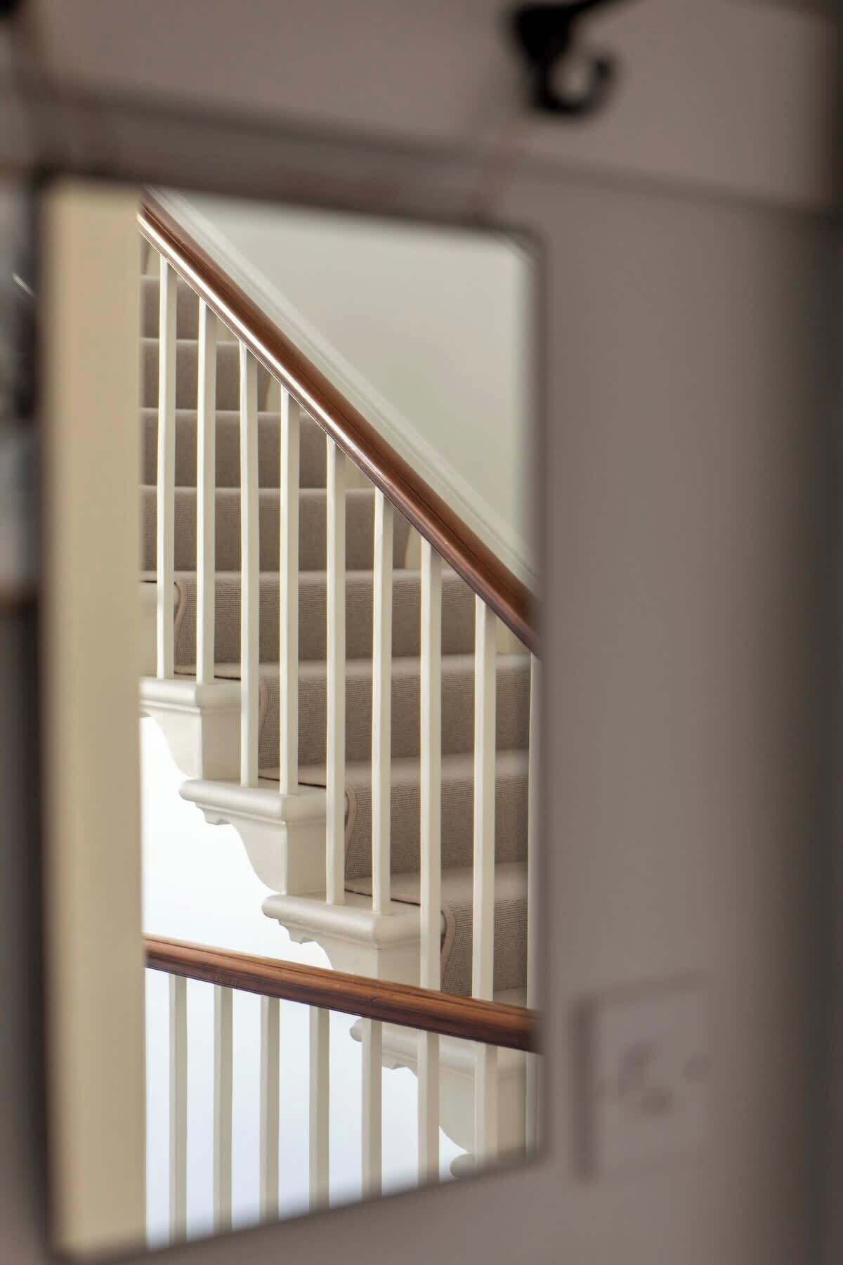 A view through a window of a staircase with white railings and a wooden handrail.