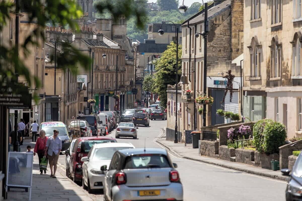 Une vue de rue avec des voitures garées, des piétons et des immeubles abritant des commerces.