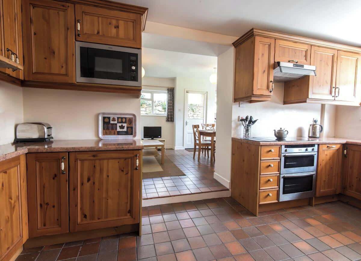 Een keuken met houten kastjes, een magnetron, een oven en een eethoek met een tafel en stoelen.