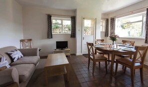 A living room with a sofa, a TV, a dining table set for six, and a window with curtains.