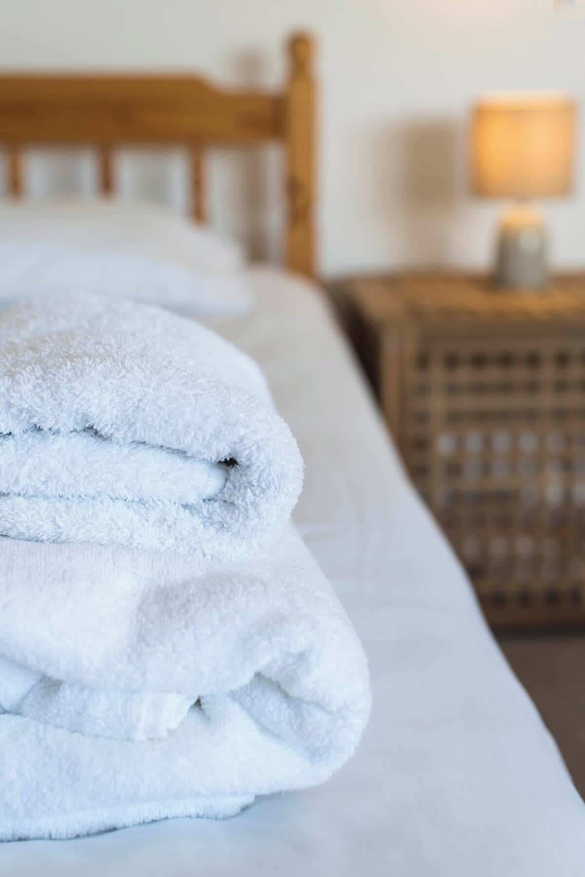 Een net opgemaakt bed met een witte deken en een gevouwen witte handdoek erop.