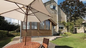 A patio with a round wooden table and chairs, an umbrella, and a stone building in the background.