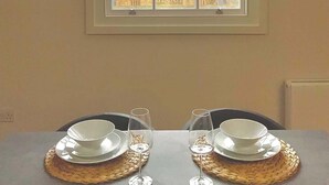 A dining area with a table set for two, a window with a view of a historic building, and a triangular ceiling design.