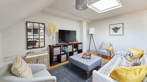 A living room with a sofa, ottoman, and a television on a wooden stand.