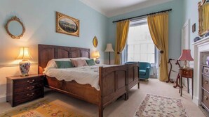 A bedroom with a wooden bed, a nightstand with a lamp, a chair, and a dresser. - Luxury Apartment Next to Bath Abbey & Shops (Bath)