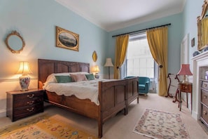 A bedroom with a wooden bed, a nightstand with a lamp, a chair, and a dresser.