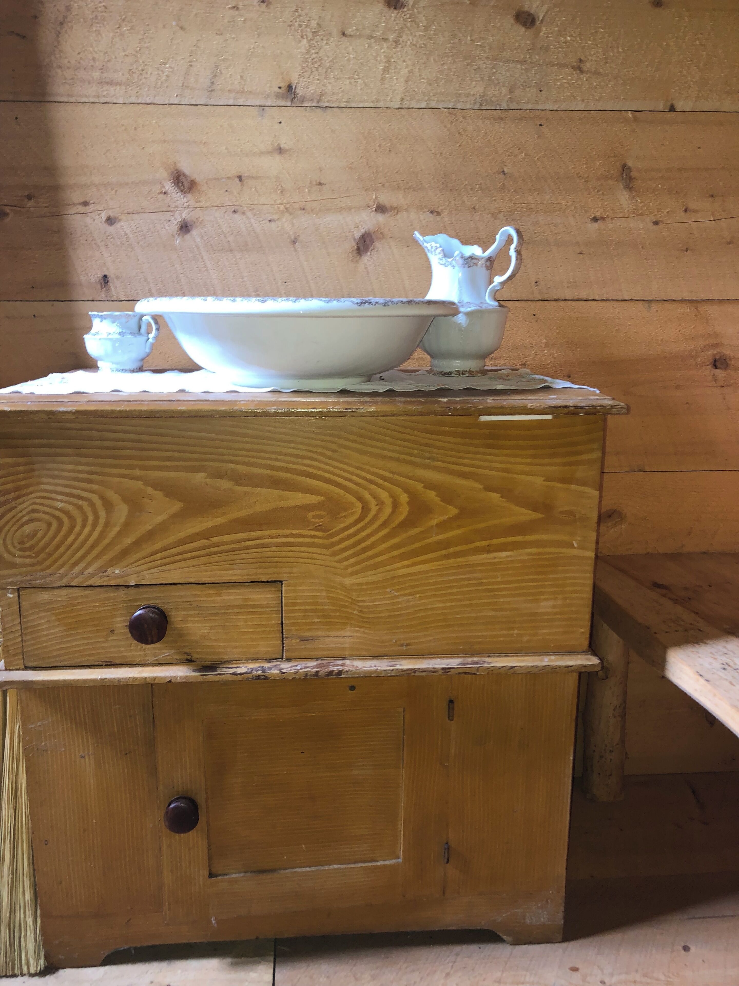 A wooden chest of drawers with a white ceramic jug and bowl on top.