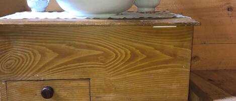 A wooden chest of drawers with a white ceramic jug and bowl on top.