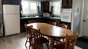 A kitchen with a wooden dining table and chairs, a refrigerator, a microwave, and cabinets. - Great Escape Cabins: Cabin 5 (Alban)