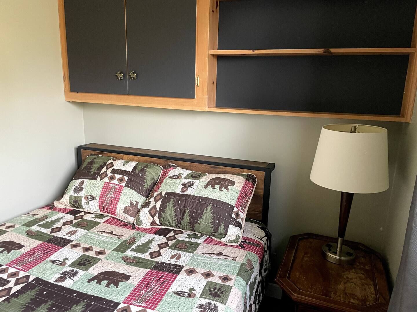 Una cama con un edredón estampado, una lámpara de noche y un mueble de madera sobre la cama.