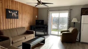 A living room with a sofa, armchair, coffee table, TV, and a sliding glass door to a deck. - Great Escape Cabins: Cabin 5 (Alban)