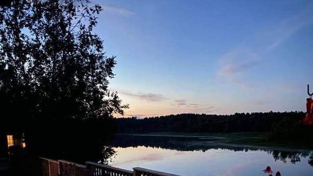 A lakeside deck with a wooden railing, surrounded by flowering plants and illuminated by lanterns. - Great Escape Cabins: Cabin 5 (Alban)