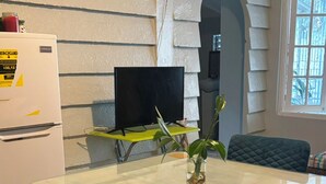Una cocina con una mesa de comedor, sillas, un refrigerador, un televisor y una ventana con vistas.