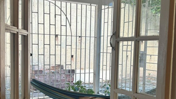 Una habitación con un ventanal grande, una hamaca y un tapete estampado.