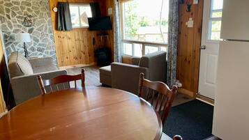 L’intérieur d’un chalet accueillant, avec un mur en pierre, un plafond en bois, une table à manger avec des chaises, un canapé, un téléviseur et une cheminée.