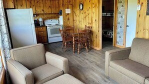 A cozy cabin interior with a dining area, wooden walls, a refrigerator, and a stone wall entrance.