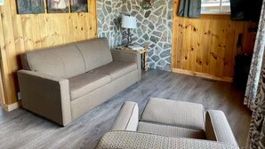 A cozy cabin interior with a sofa, a small table with a lamp, and a stone wall.